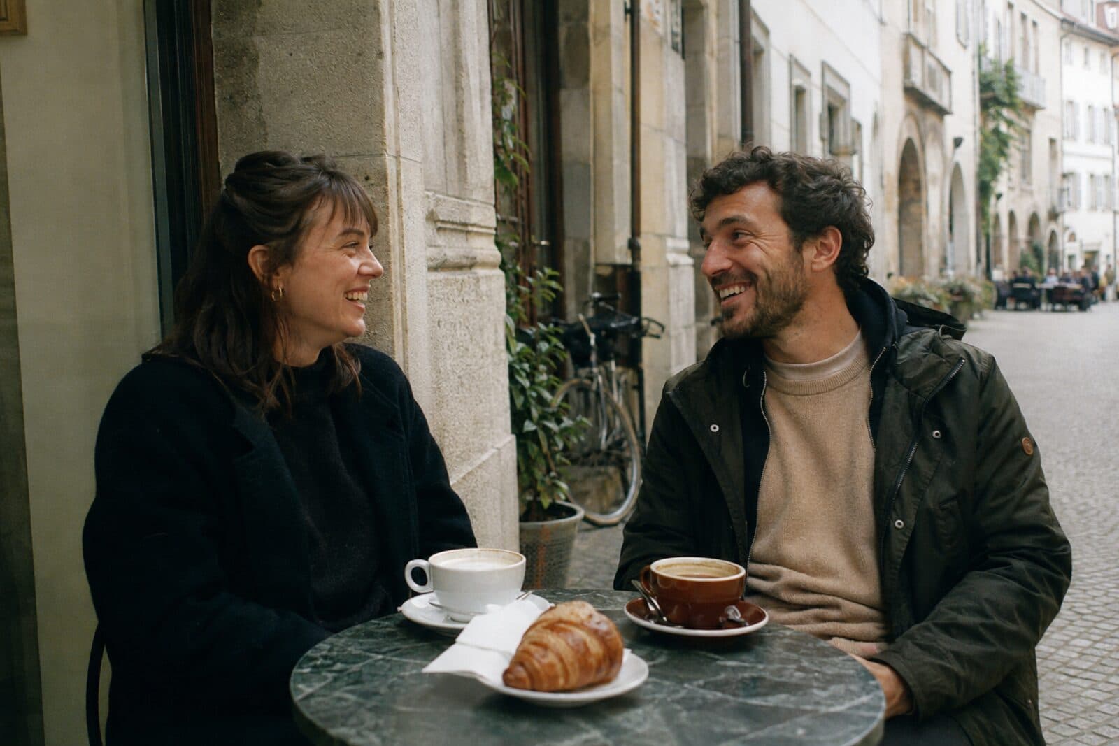 Zwei Freunde lachen bei einem Kaffee vor einem Café in der Altstadt