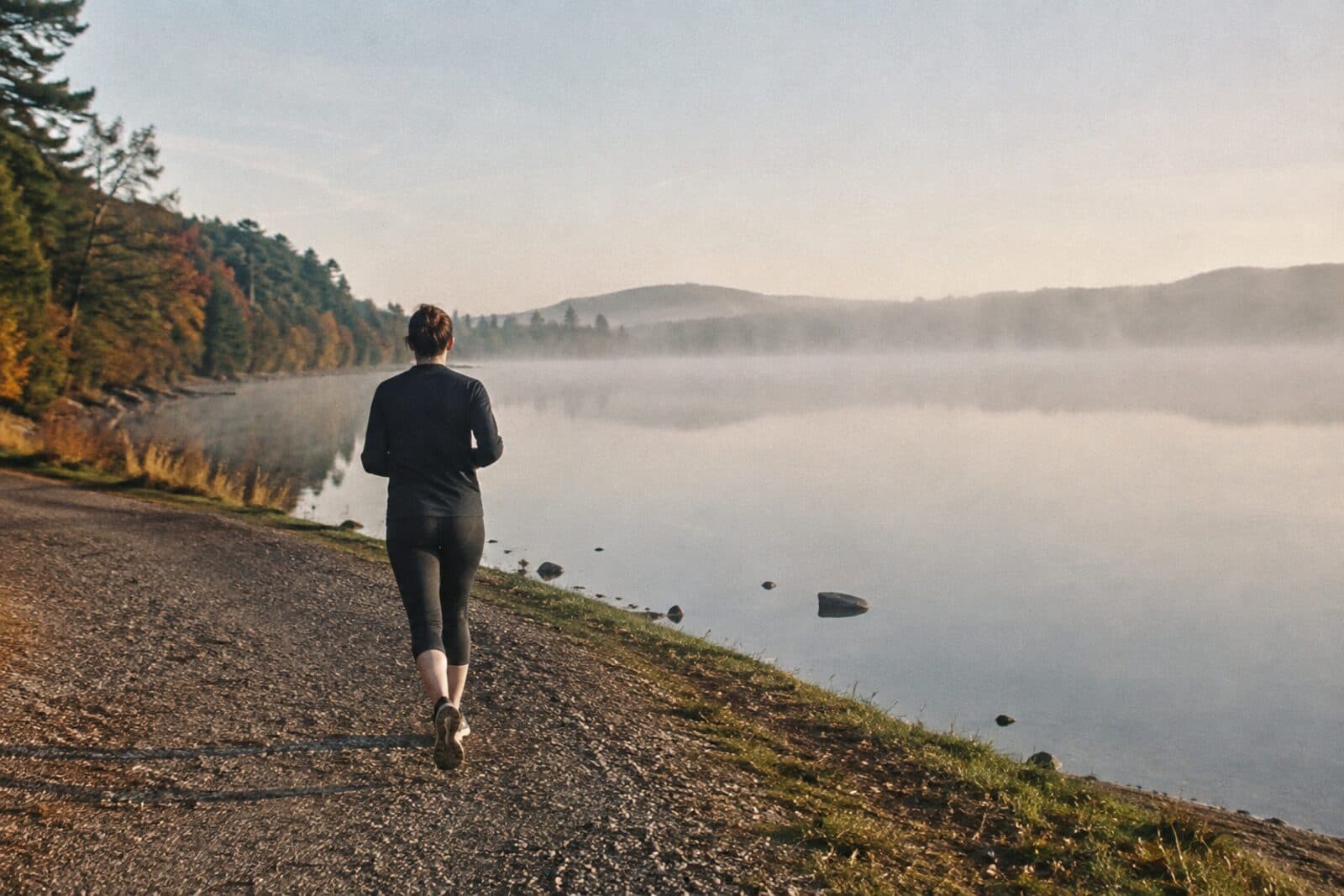 Eine Läuferin auf einem Uferweg am frühen Morgen