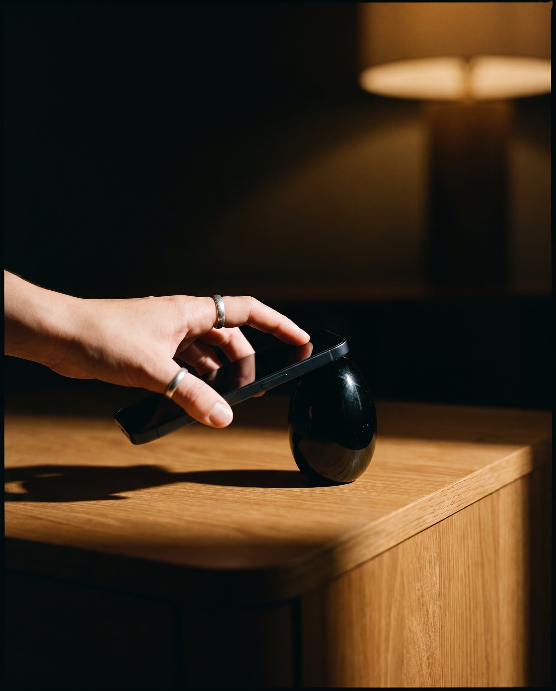 Eine Hand hält ein Smartphone ans schwarze Yeara Ei auf einem Holztisch